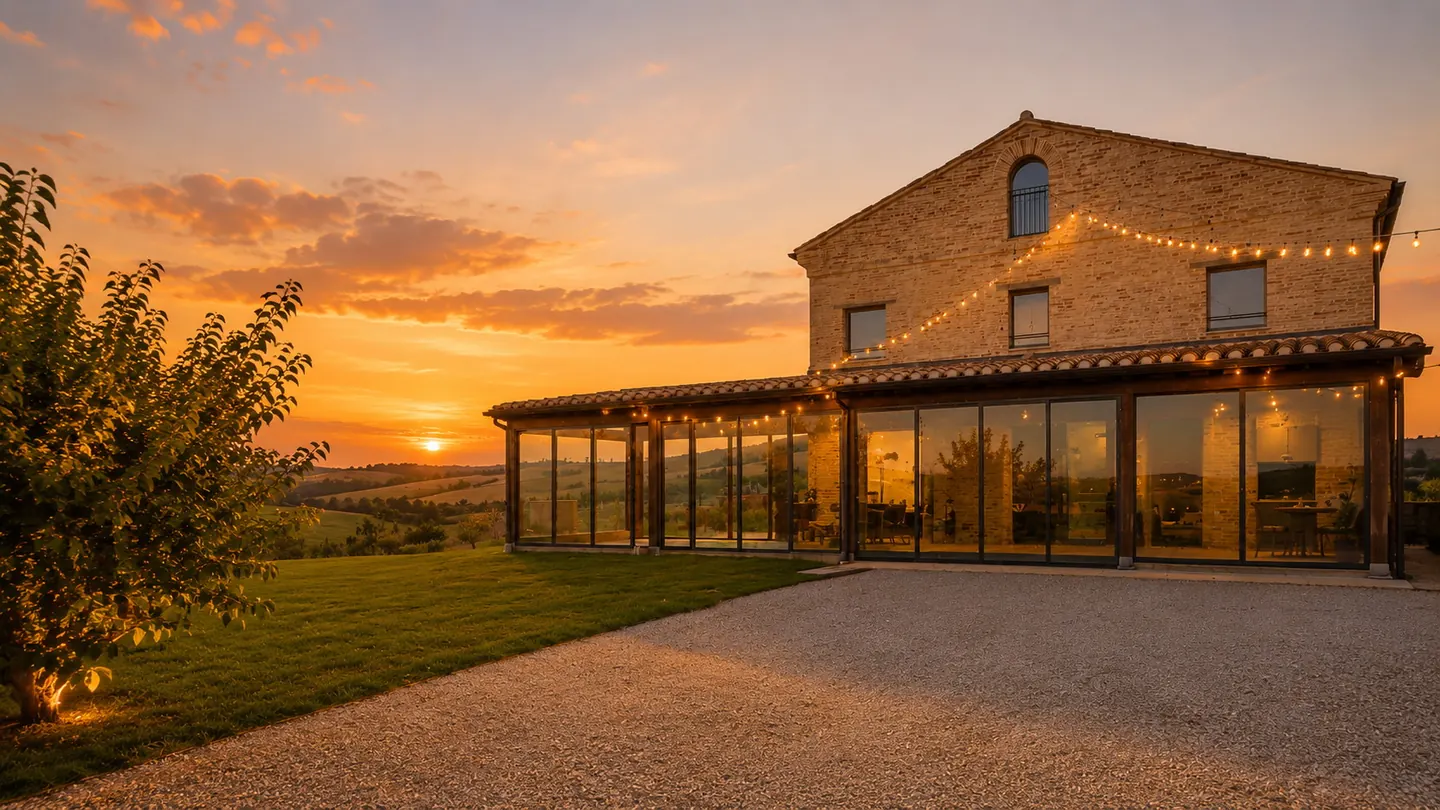 Il casale di Calamonte al tramonto, con la veranda vetrata illuminata e le colline sullo sfondo